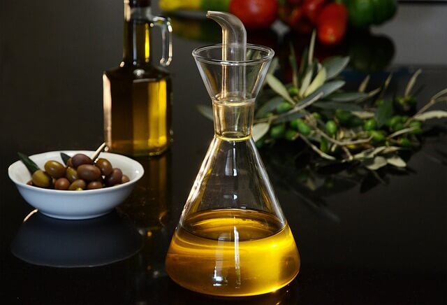 Sunnah Foods & Their Modern Health Benefits 6 Extra virgin olive oil in a glass bottle next to fresh green olives on a wooden table