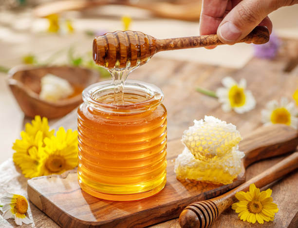 Sunnah Foods & Their Modern Health Benefits 3 Golden honey dripping from a spoon into a glass jar, symbolizing healing in Islam